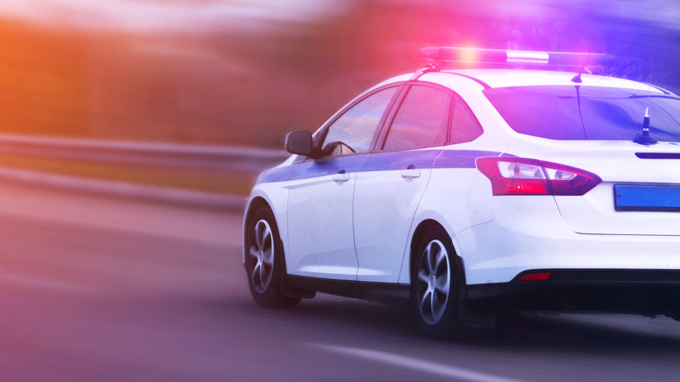 Carro de polícia descendo a rua em alta velocidade com as luzes piscando